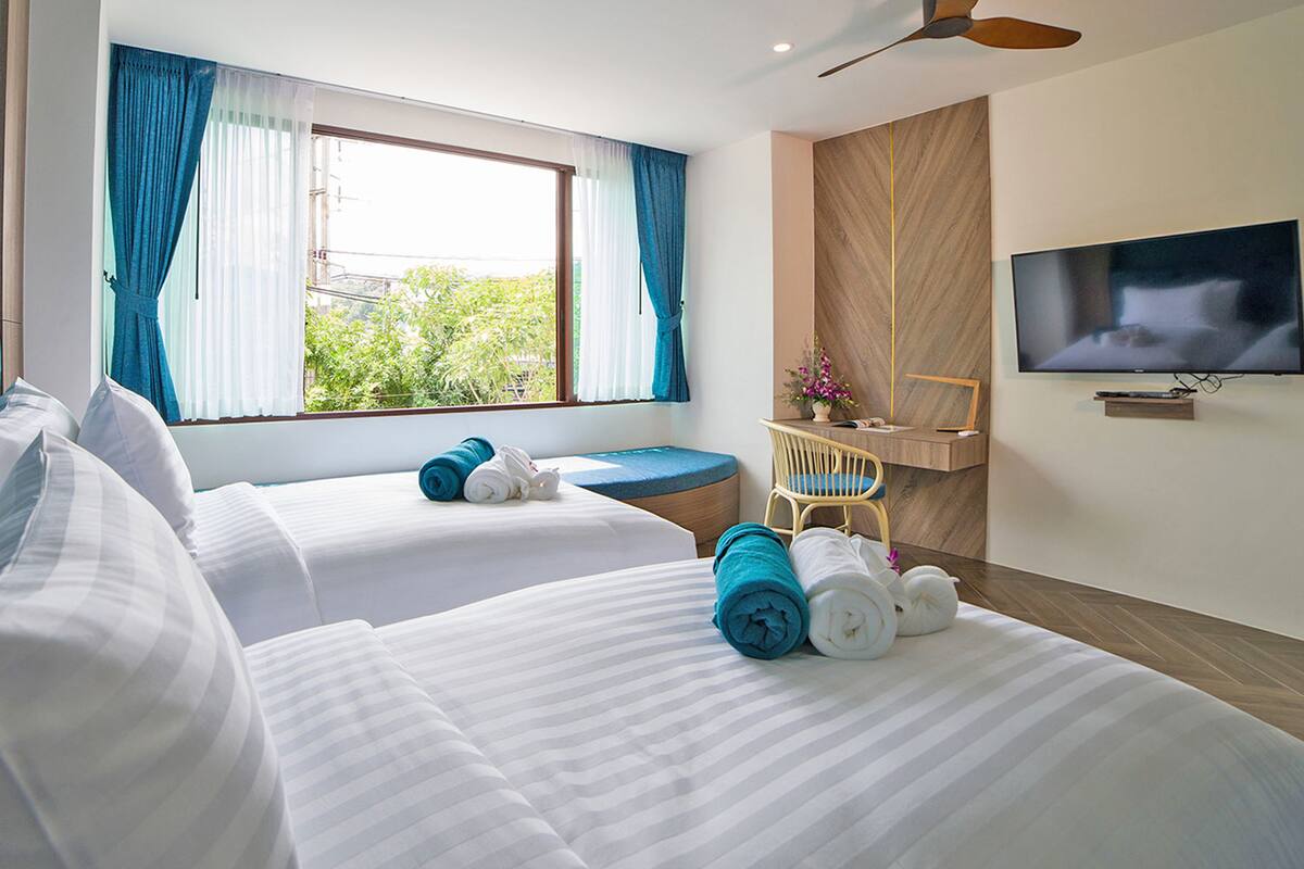 A hotel room with two beds, a TV, a desk, and a window with curtains.