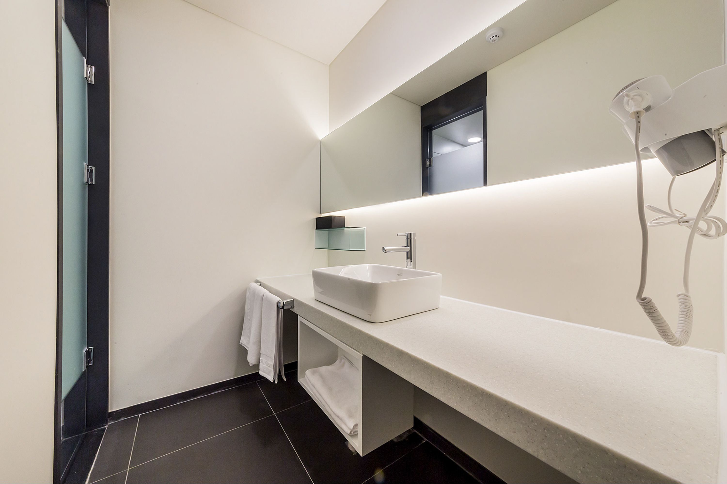 Une salle de bain moderne avec un lavabo blanc, un porte-serviettes, un miroir et un sèche-cheveux.