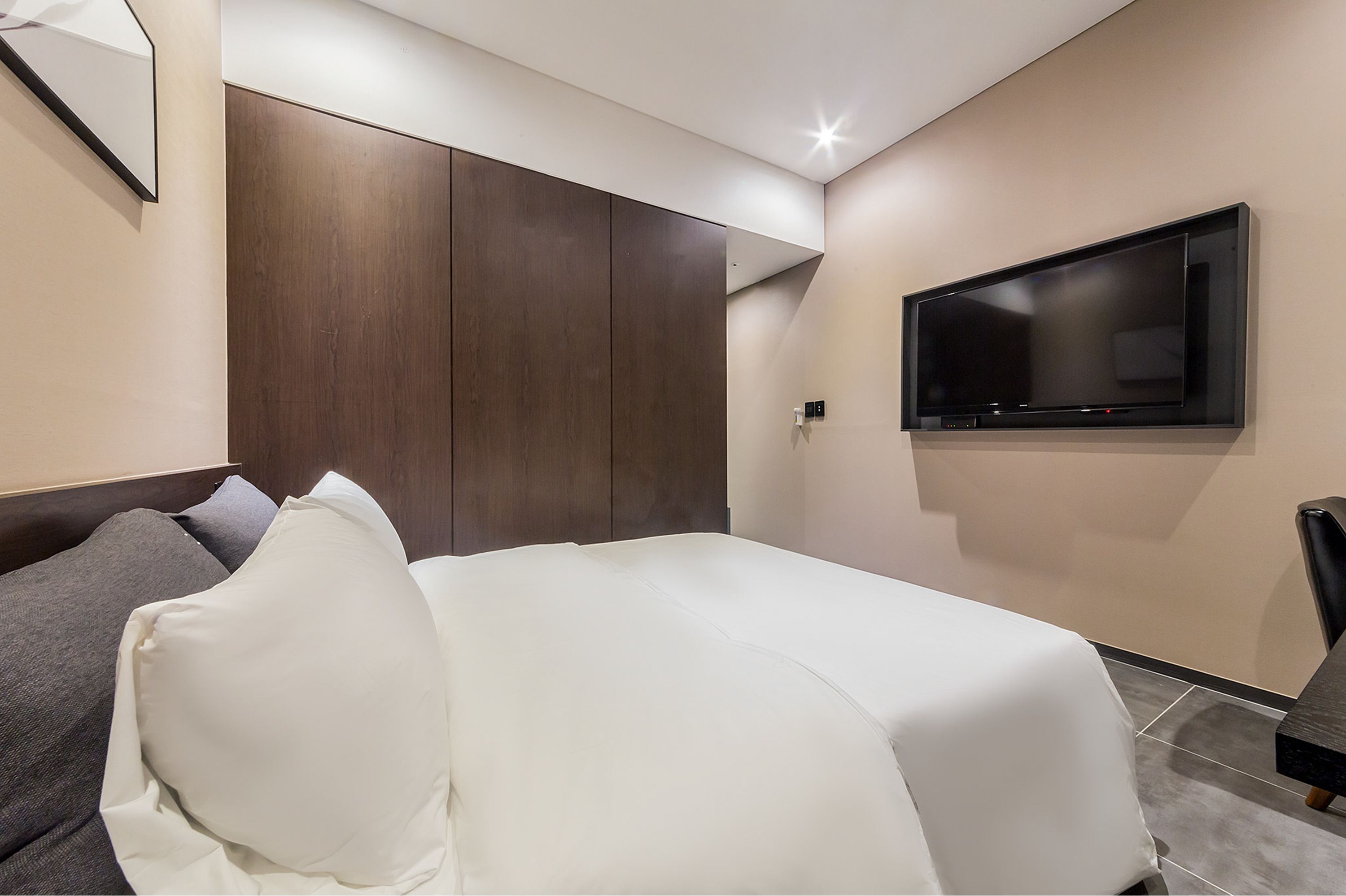 A modern hotel room with a bed, a TV mounted on the wall, and a wardrobe.
