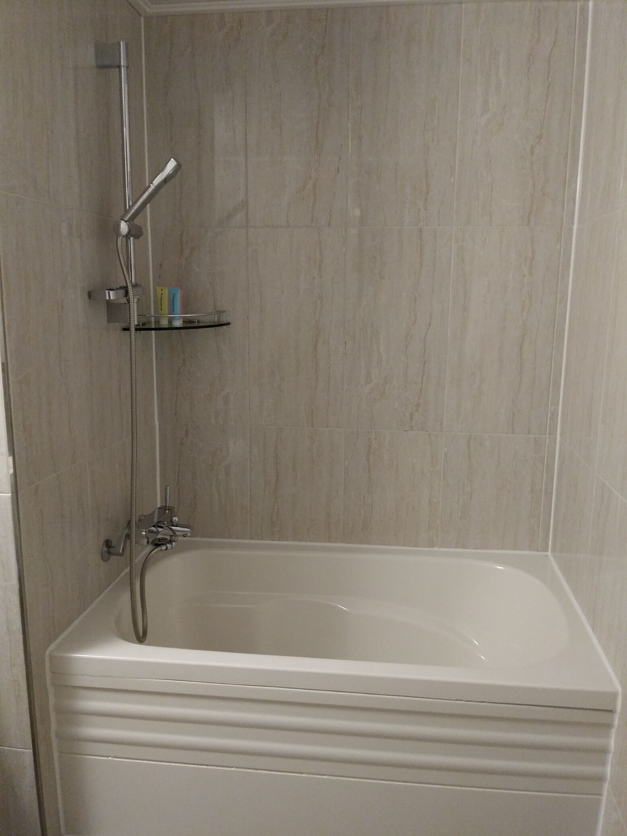 Un baño con bañera, ducha y repisa de vidrio con artículos de aseo.