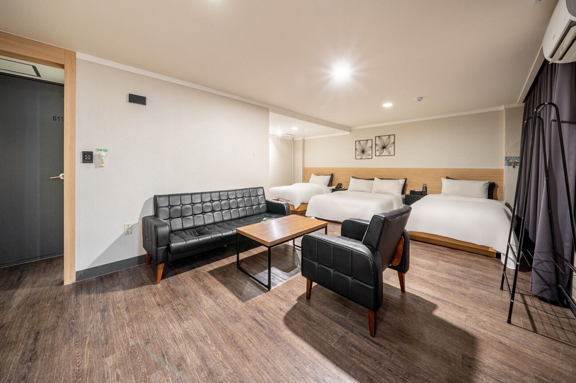 A hotel room with a sofa, two single beds, a small table, and a chair.