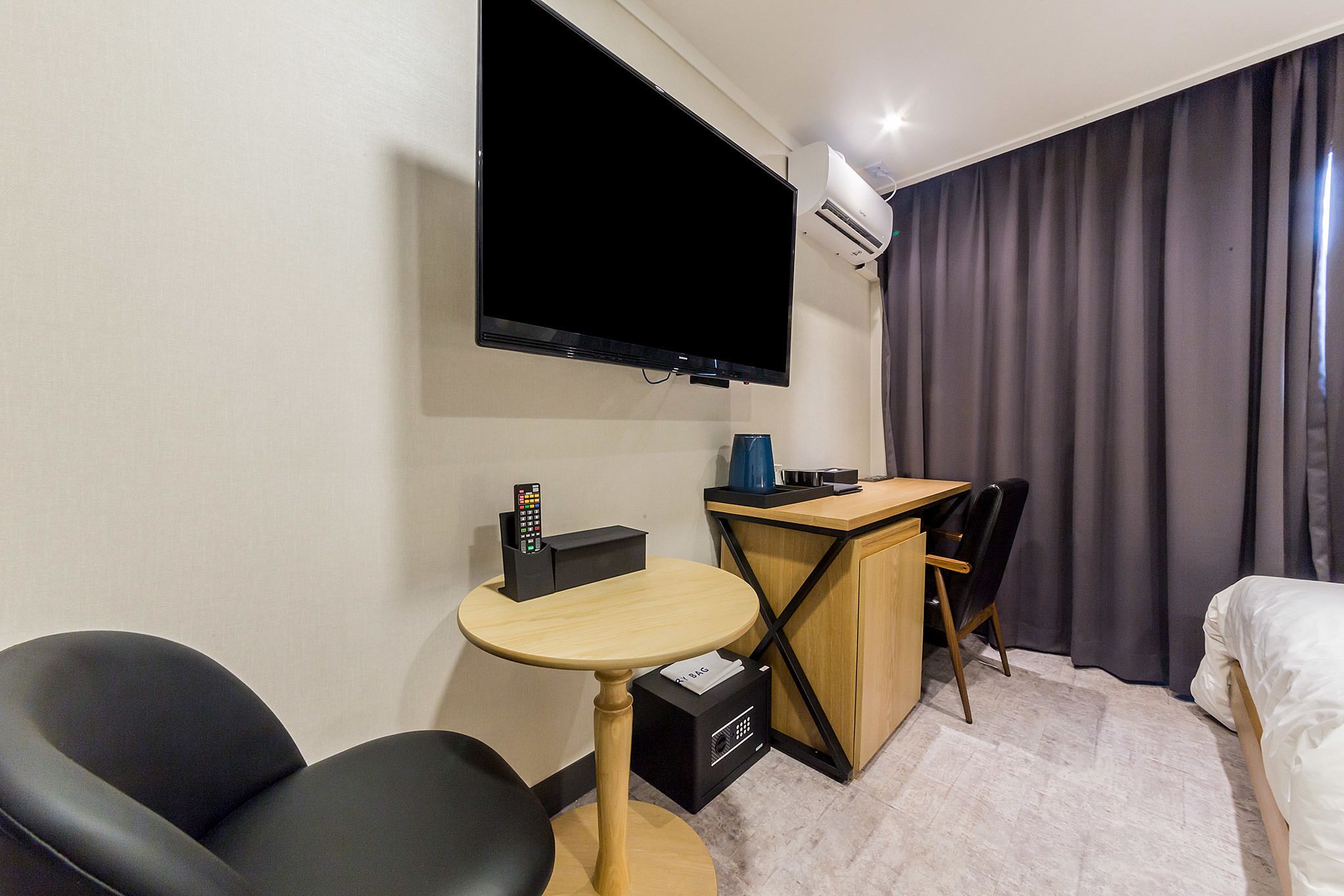 Habitación de hotel con televisión de pantalla plana en la pared, un escritorio con silla, cama y una mesita con el control remoto.