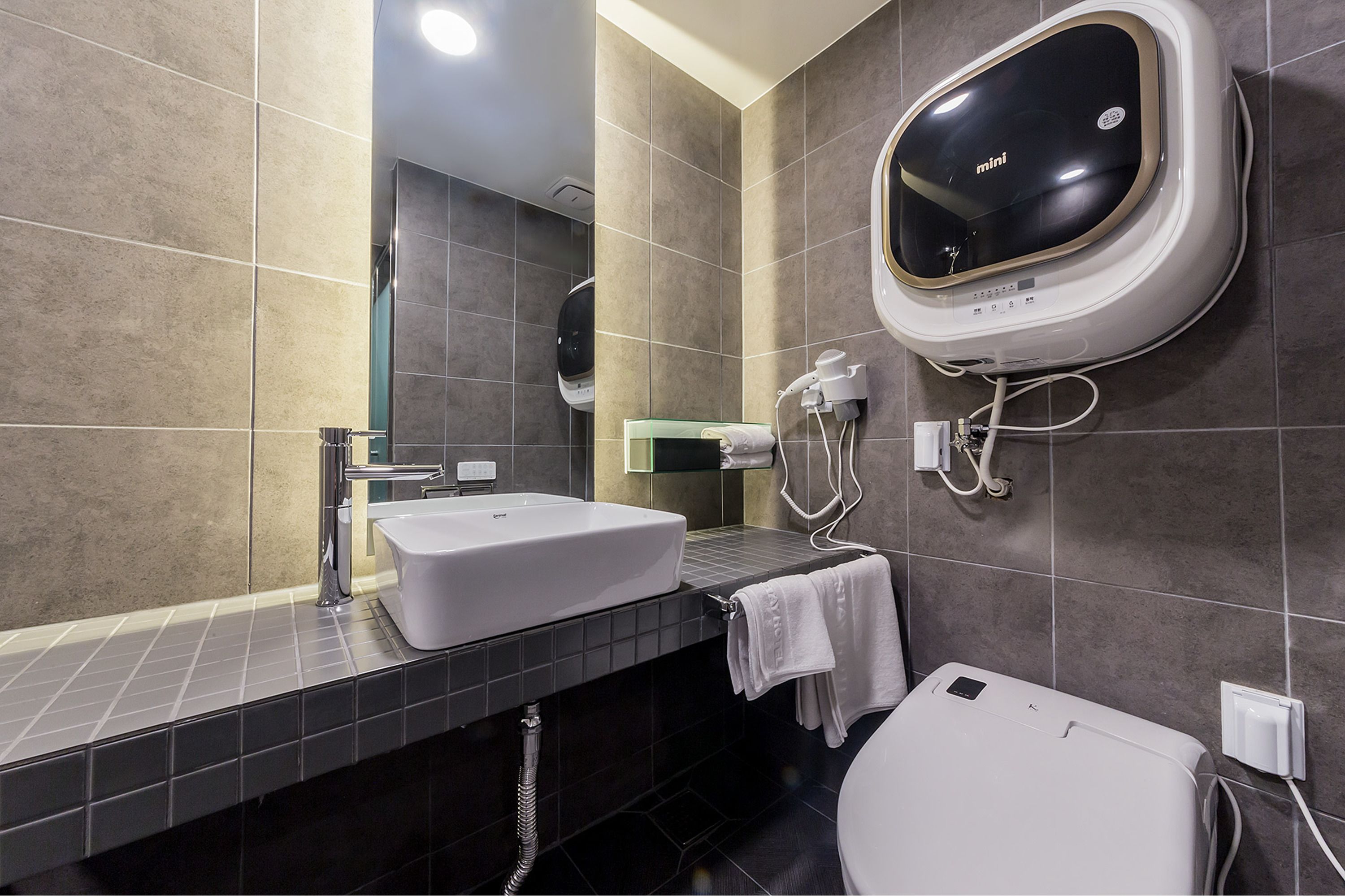 A modern bathroom with a white sink, a mirror, a toilet, and a wall-mounted hand dryer.
