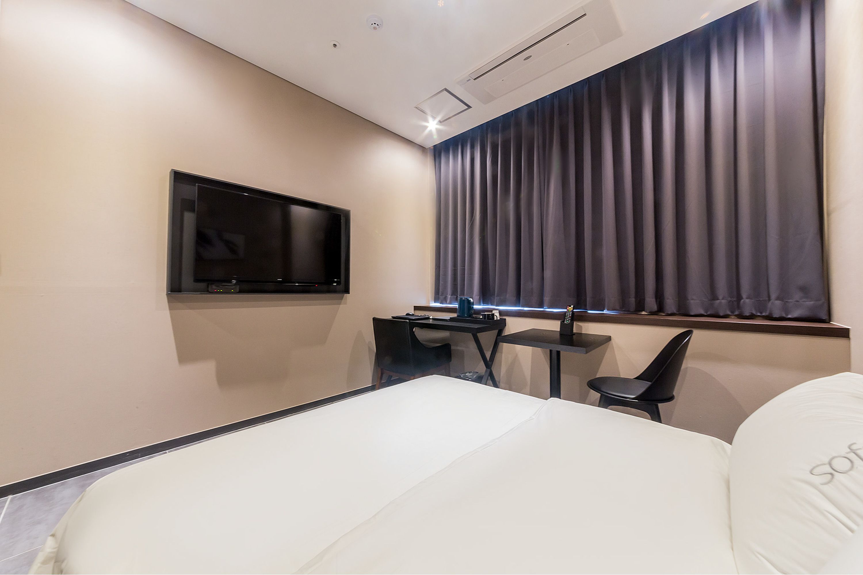 A modern hotel room with a bed, a desk, a chair, a TV, and a window with curtains.