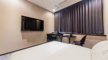 A modern hotel room with a bed, a desk, a chair, a TV, and a window with curtains.