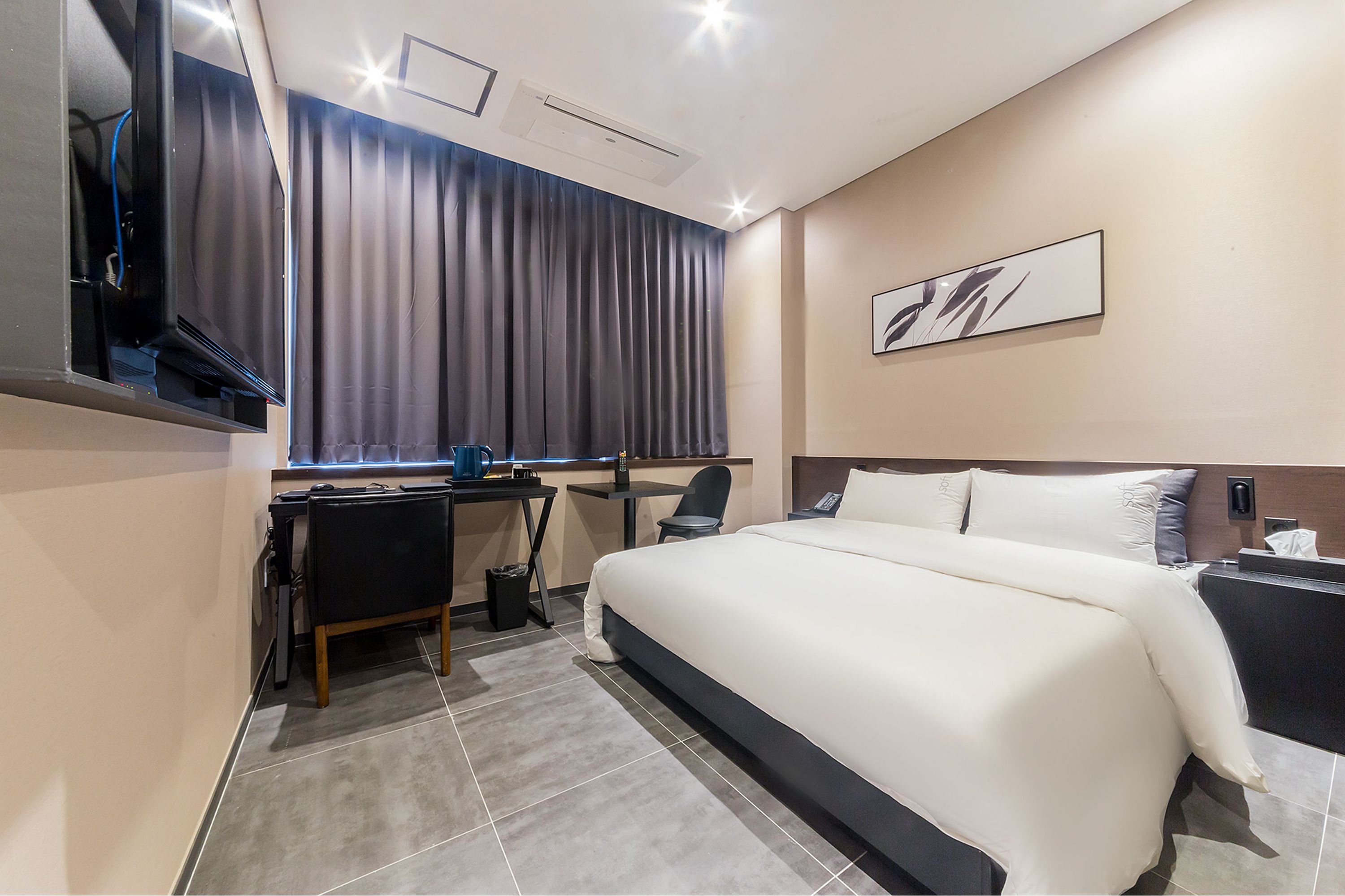 Habitación de hotel moderna con una cama grande, un escritorio con silla, un televisor de pantalla plana y un amplio ventanal con cortinas.