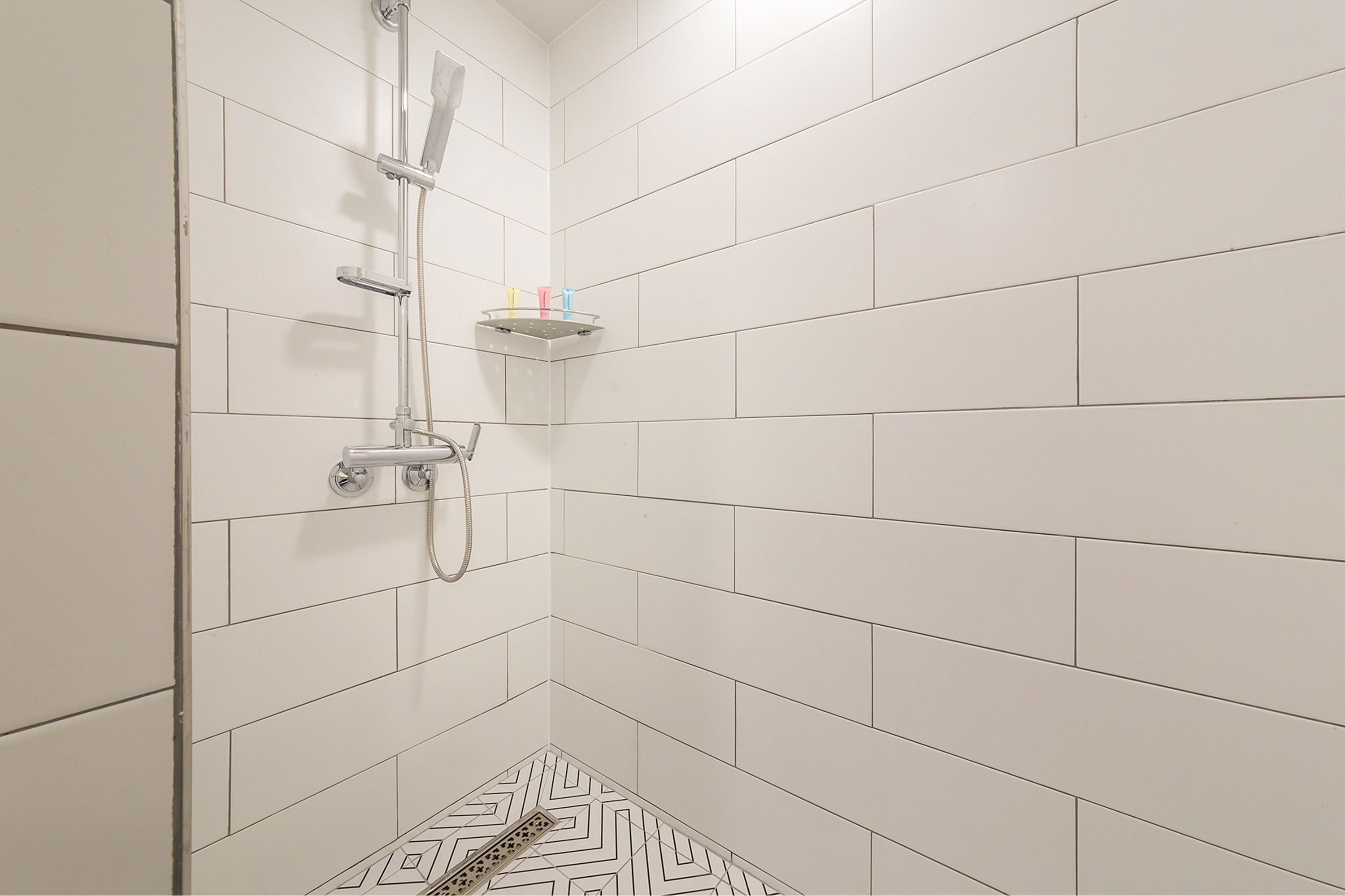 Un baño pequeño con azulejos blancos, ducha de mano y grifo empotrado.
