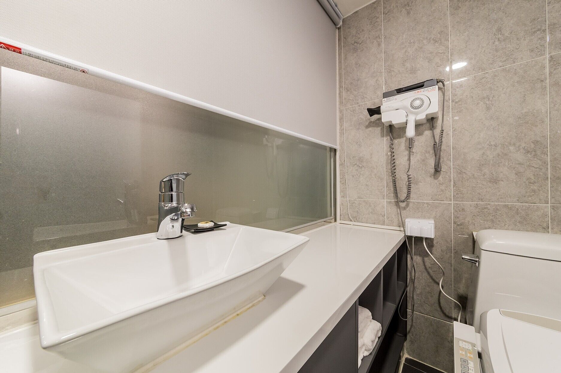 A modern bathroom with a white sink, a glass shower enclosure, and a hairdryer mounted on the wall.