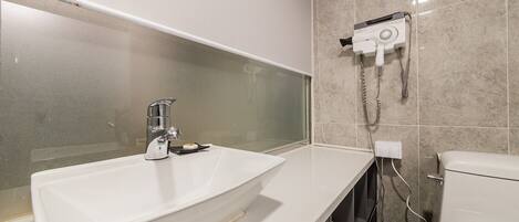 A modern bathroom with a white sink, a glass shower enclosure, and a hairdryer mounted on the wall.