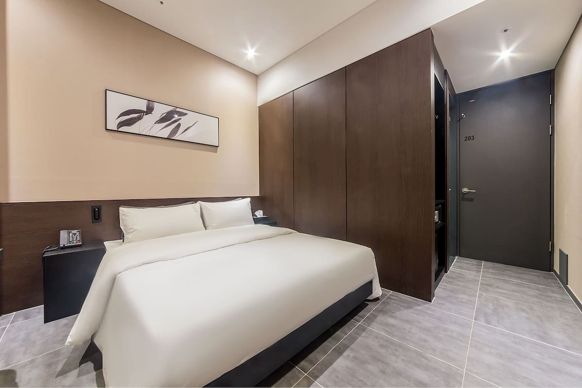 A modern hotel room with a large bed, a dark wooden wardrobe, and a framed artwork on the wall.