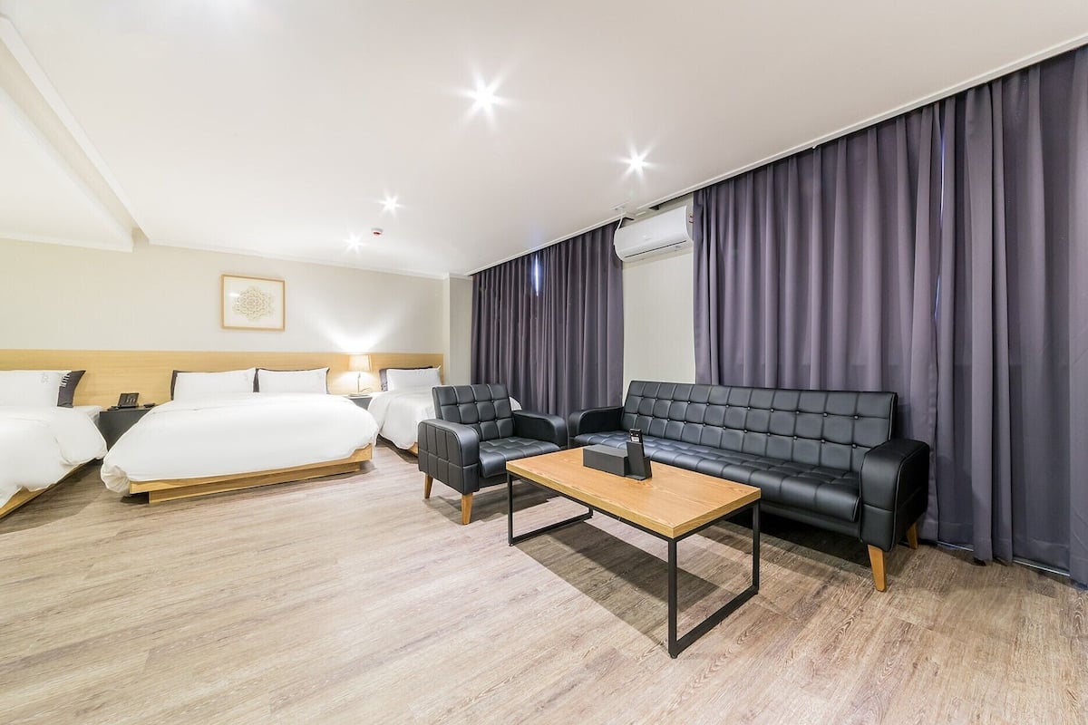 A hotel room with a bed, two armchairs, a sofa, a coffee table, and a large window with curtains.