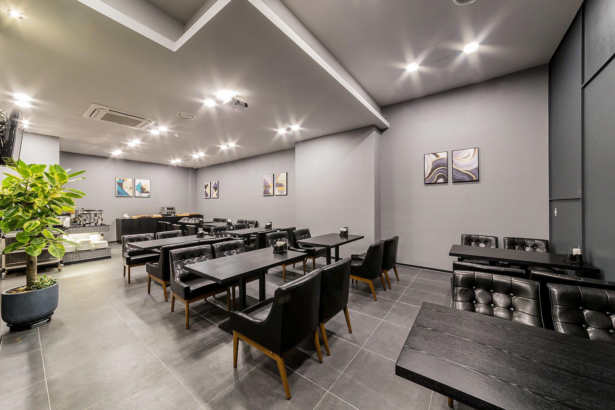 A modern dining area with multiple tables and chairs, a potted plant, and artwork on the walls.