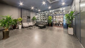 A modern lobby with a grey sofa, a coffee table, and potted plants. There is a glass display case with items and a door leading to a kitchen area. - Pyeongtaek Stay Hotel (Pyeongtaek)