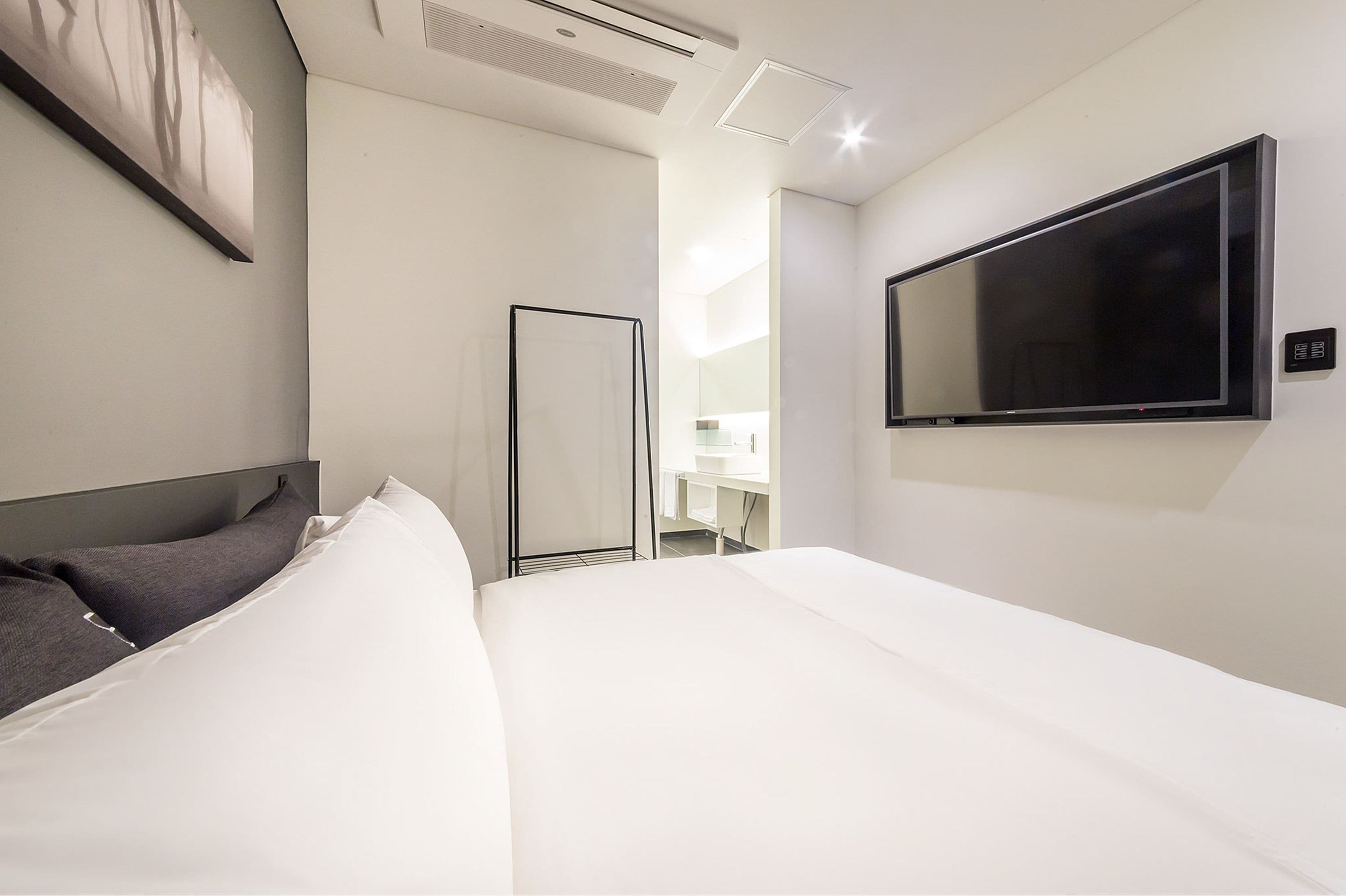 A modern hotel room with a large bed, a flat-screen TV mounted on the wall, and a walk-in closet with a mirror.