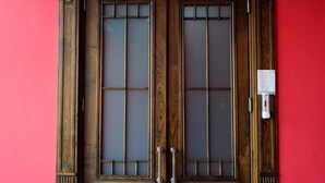 A double wooden door with glass panels and decorative elements, set against a red wall. - Hotel Monopoli Kutaisi (Kutaisi)