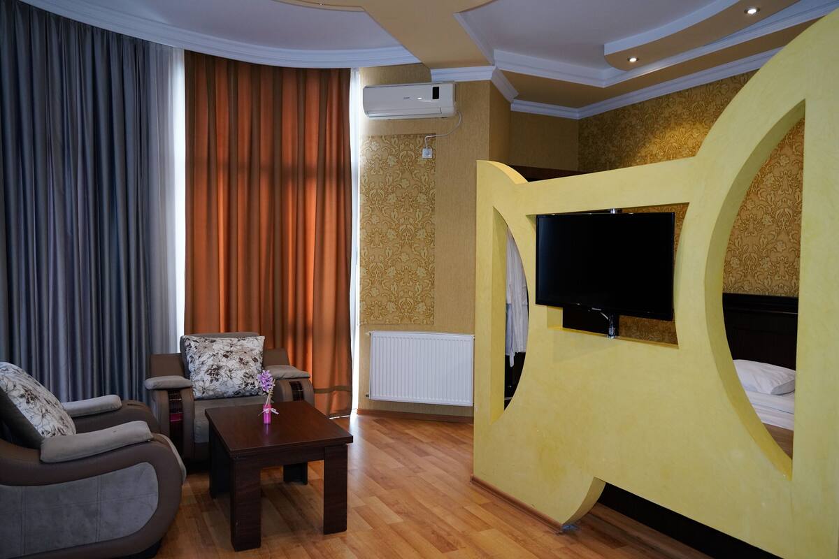 Une chambre d’hôtel comprenant un canapé, une petite table avec un vase, un lit avec un téléviseur et un grand panneau décoratif mural.