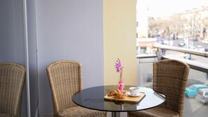 A round glass table with wicker chairs, a vase with pink flowers, a cup, and a plate with croissants. - Hotel Monopoli Kutaisi (Kutaisi)
