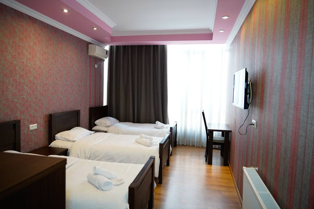 Une chambre d’hôtel avec trois lits, un bureau, une chaise et un téléviseur fixé au mur.