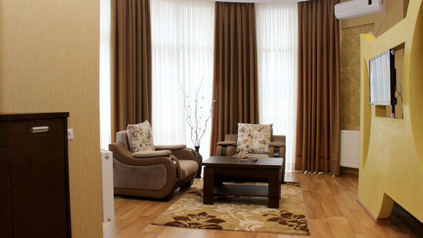 A living room with a sofa, armchair, and coffee table, a TV mounted on the wall, and a radiator. - Hotel Monopoli Kutaisi (Kutaisi)