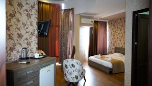 A hotel room with a bed, a desk with a kettle, a chair, a television, and a wardrobe. - Hotel Monopoli Kutaisi (Kutaisi)