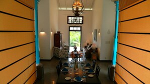 A dining area with a long table set for six, a chandelier, and a view of greenery outside. - Thompson Manor - A Luxury Villa in Galle (Akmeemana)