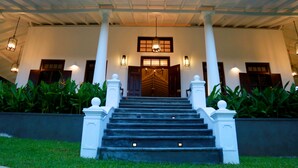 A grand entrance with a staircase leading to a wooden door, flanked by columns and lit by wall sconces. - Thompson Manor - A Luxury Villa in Galle (Akmeemana)