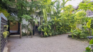 Escape to a serene courtyard surrounded by lush greenery and tropical plants, featuring a traditional-style building with a tiled roof.