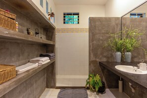 A bathroom with a shower, a sink, and a shelf with towels. - Enkosa Modern Villa (Siem Reap)