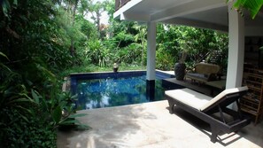 A pool area with lounge chairs and a covered seating area surrounded by lush greenery. - Enkosa Modern Villa (Siem Reap)