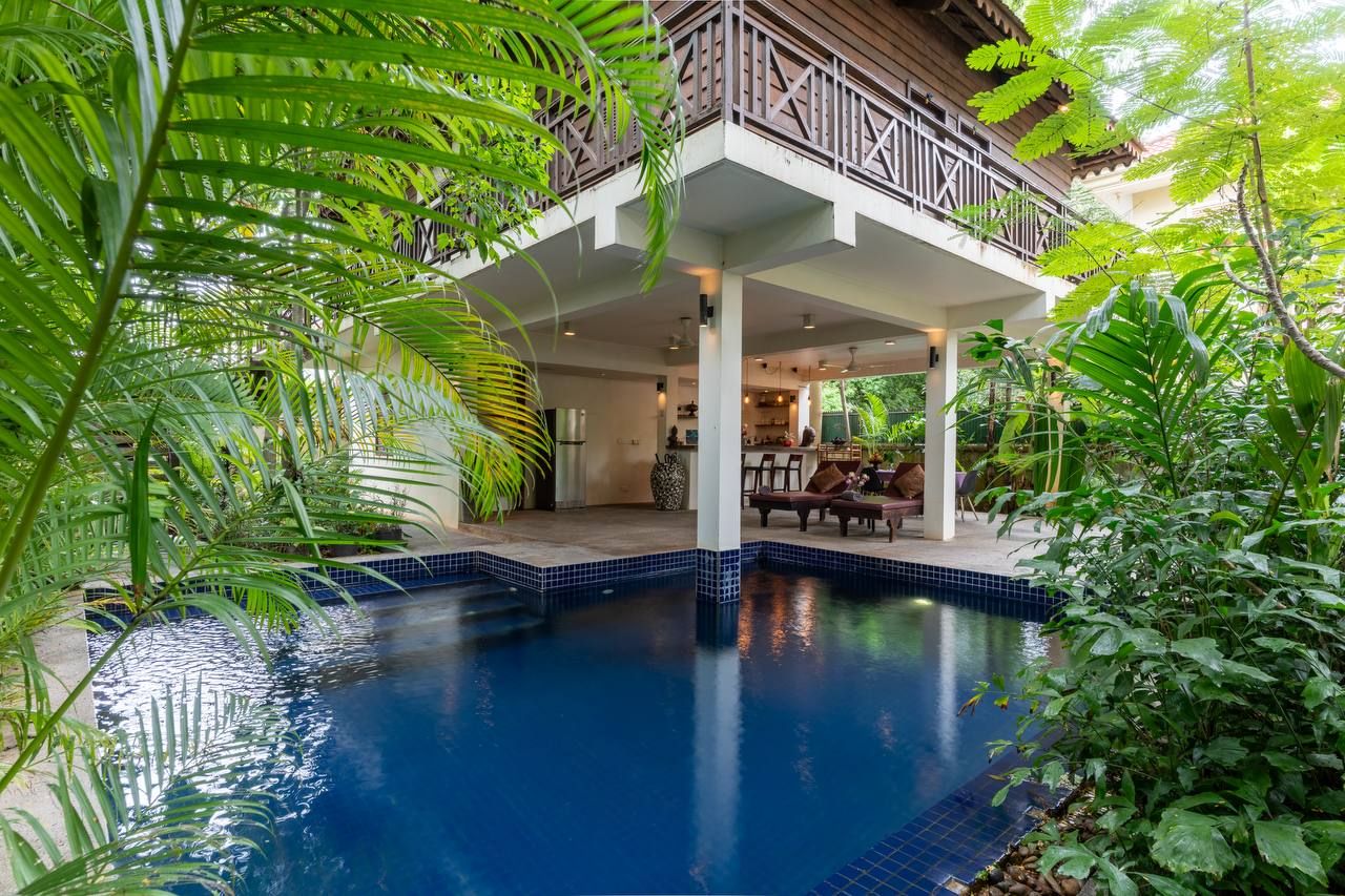 A pool with a wooden deck and lounge chairs, surrounded by lush greenery.