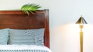 A bed with striped bedding and a wooden headboard, a green plant on the headboard, and a tall floor lamp with a conical shade. - Inje Tourist Hotel (Inje)