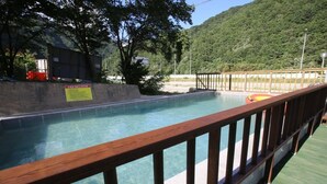 A swimming pool with a wooden deck and a view of a forested hillside. - Inje Tourist Hotel (Inje)