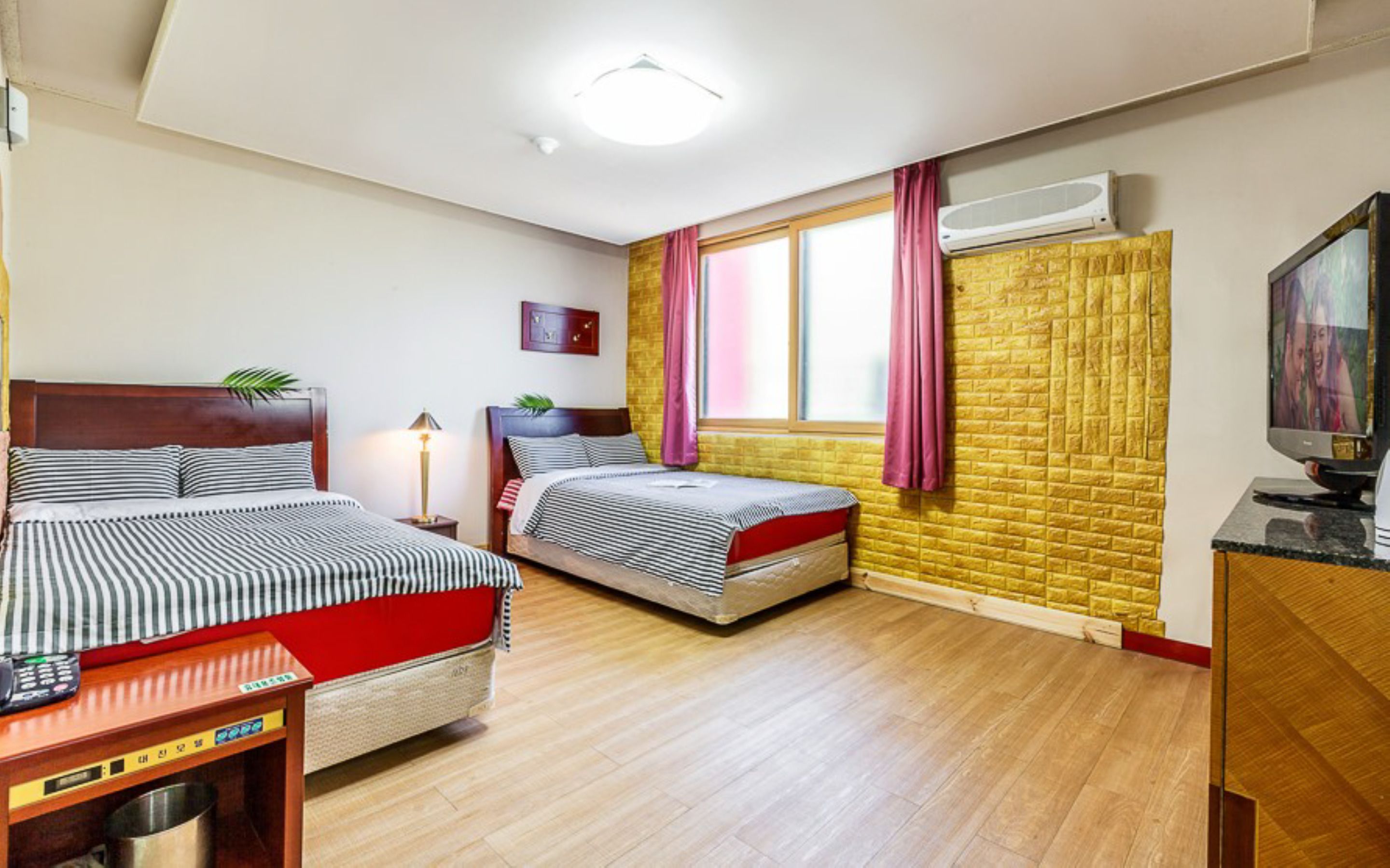 A hotel room with two beds, a TV, a desk, and a window with curtains.