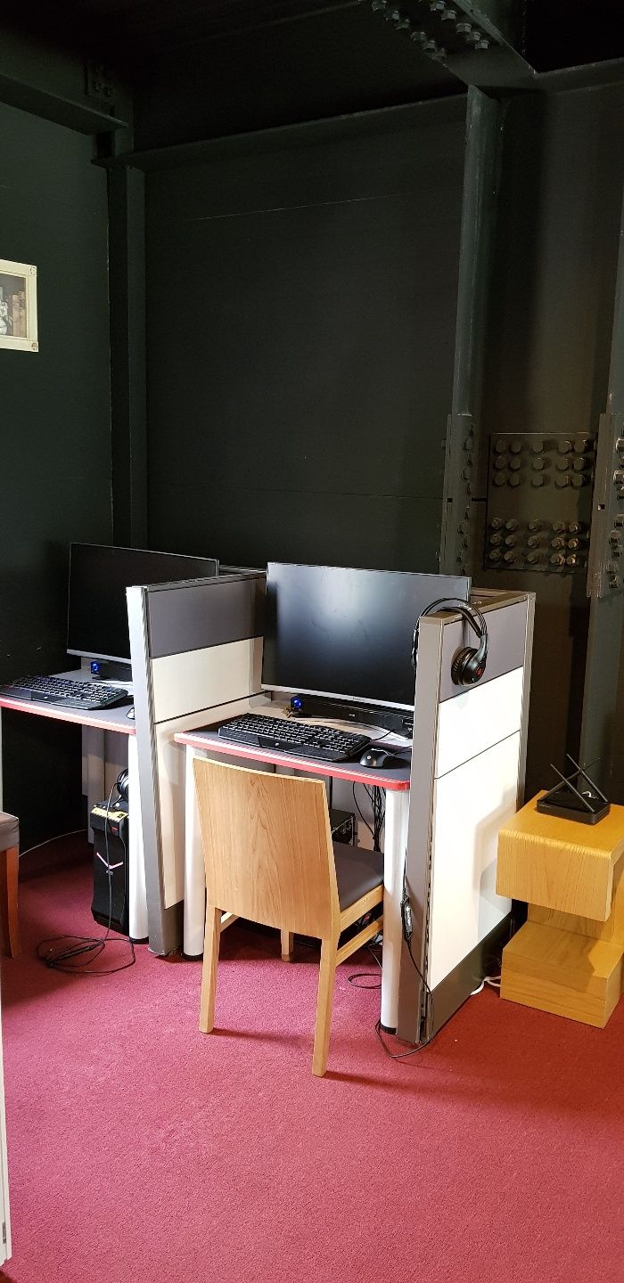Ein Zimmer mit Schreibtisch, Computer und einer kleinen Holzbank.