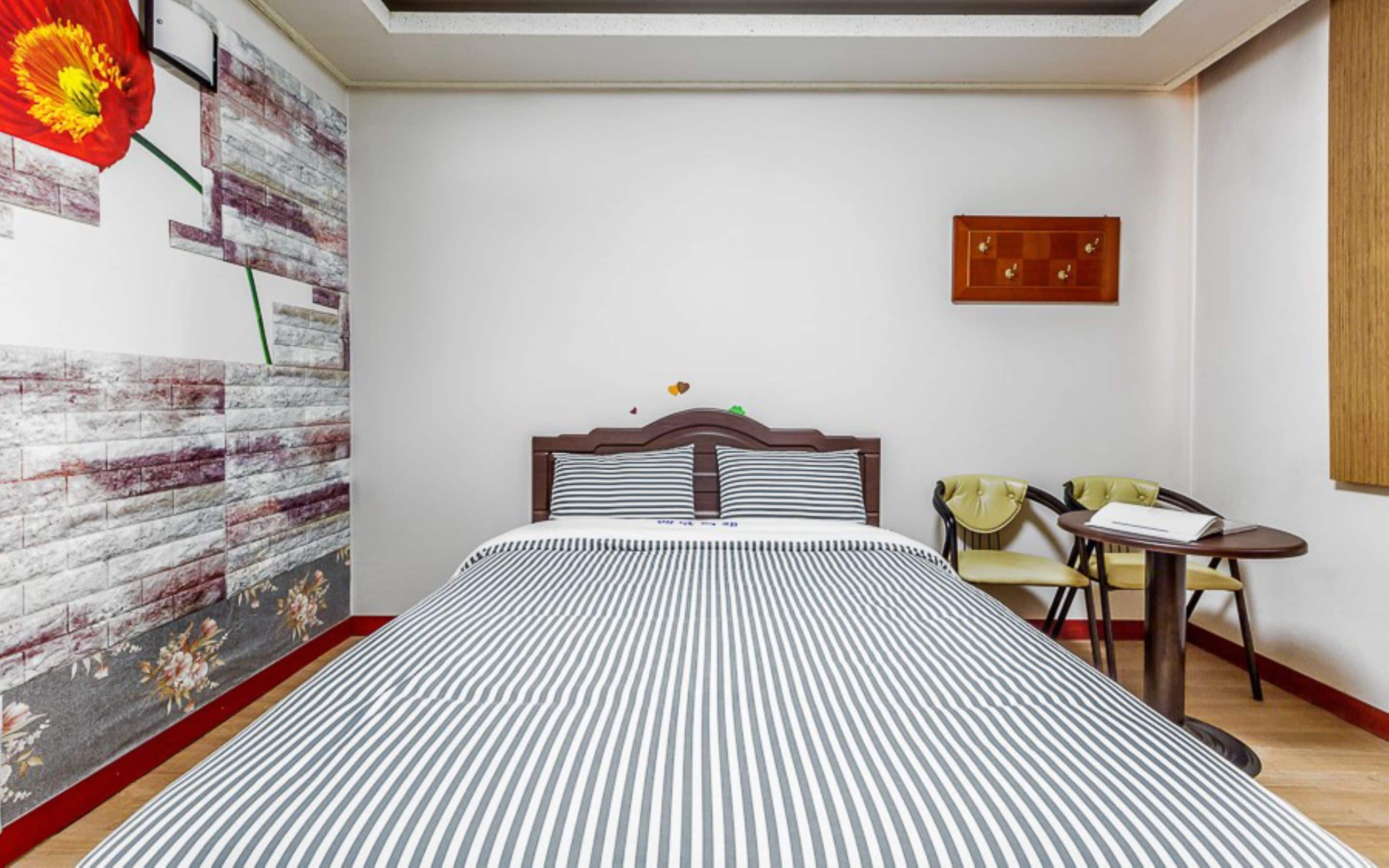 Une chambre d’hôtel avec un lit, une petite table et des chaises, une horloge murale et une fleur décorative accrochée au mur.