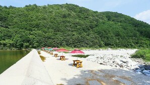 Un muelle de hormigón que se adentra en el agua, con taburetes de madera y sombrillas rojas.