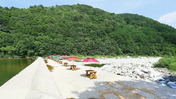 A concrete pier extending into a body of water, lined with wooden stools and red umbrellas. - Inje Tourist Hotel (Inje)