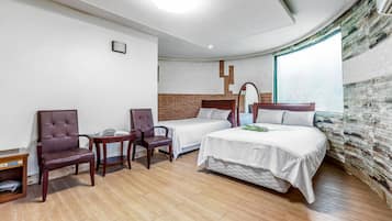 A hotel room with two single beds, a wooden floor, a brick accent wall, and a large window.