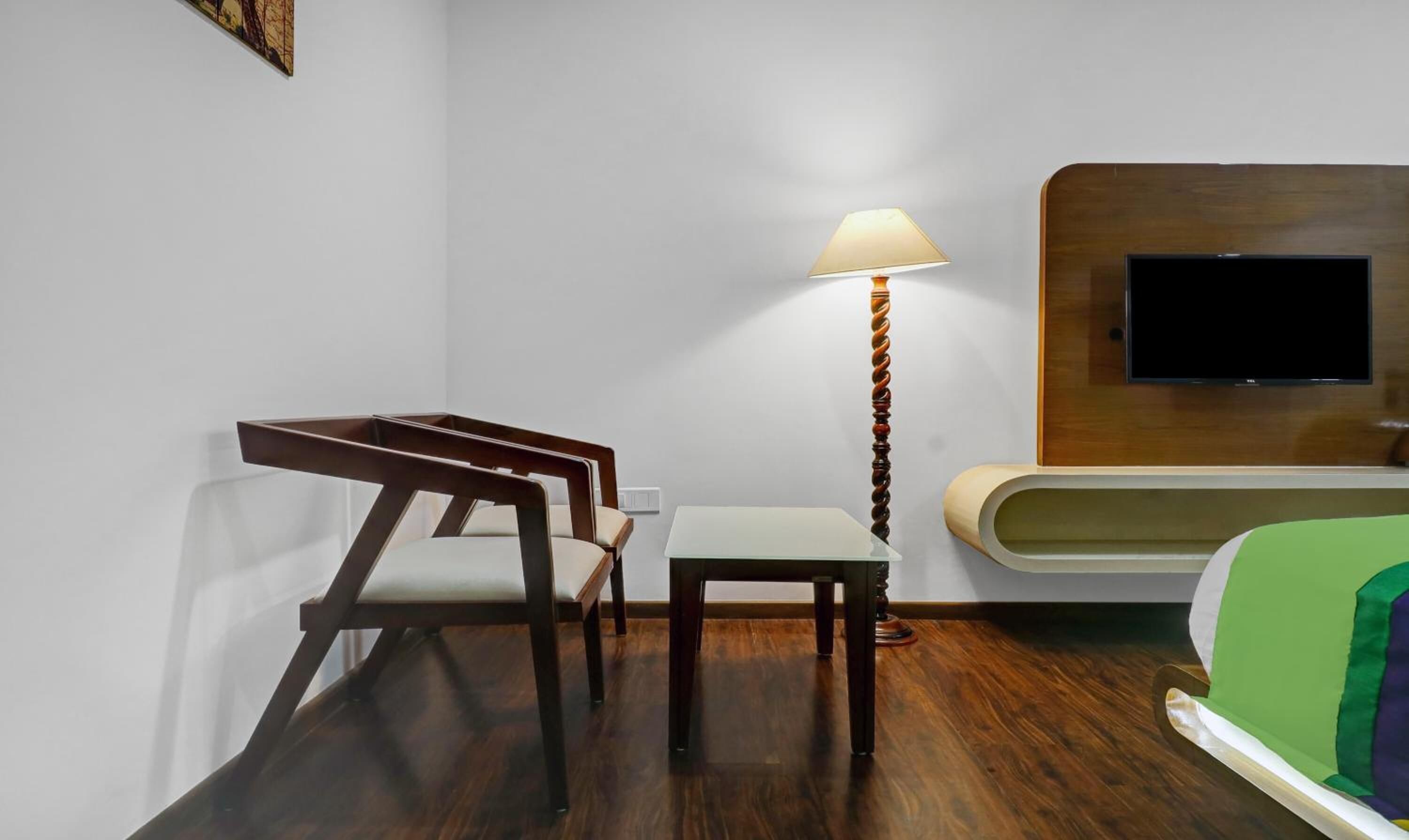 Une chambre d’hôtel équipée d’un lit, d’un bureau, de deux chaises, d’une lampe et d’un téléviseur fixé au mur.