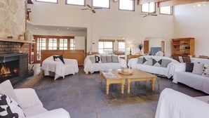 Een ruime woonkamer met een open haard, diverse zithoeken en grote ramen voor natuurlijk licht.