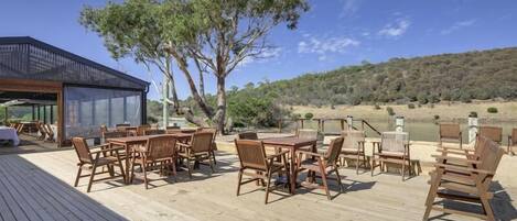 A wooden deck with outdoor seating, a glass-enclosed area, and a view of a river and hills.