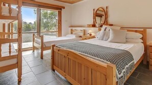 Een slaapkamer met een houten bed, een nachtkastje, een spiegel en een raam met uitzicht op groen.