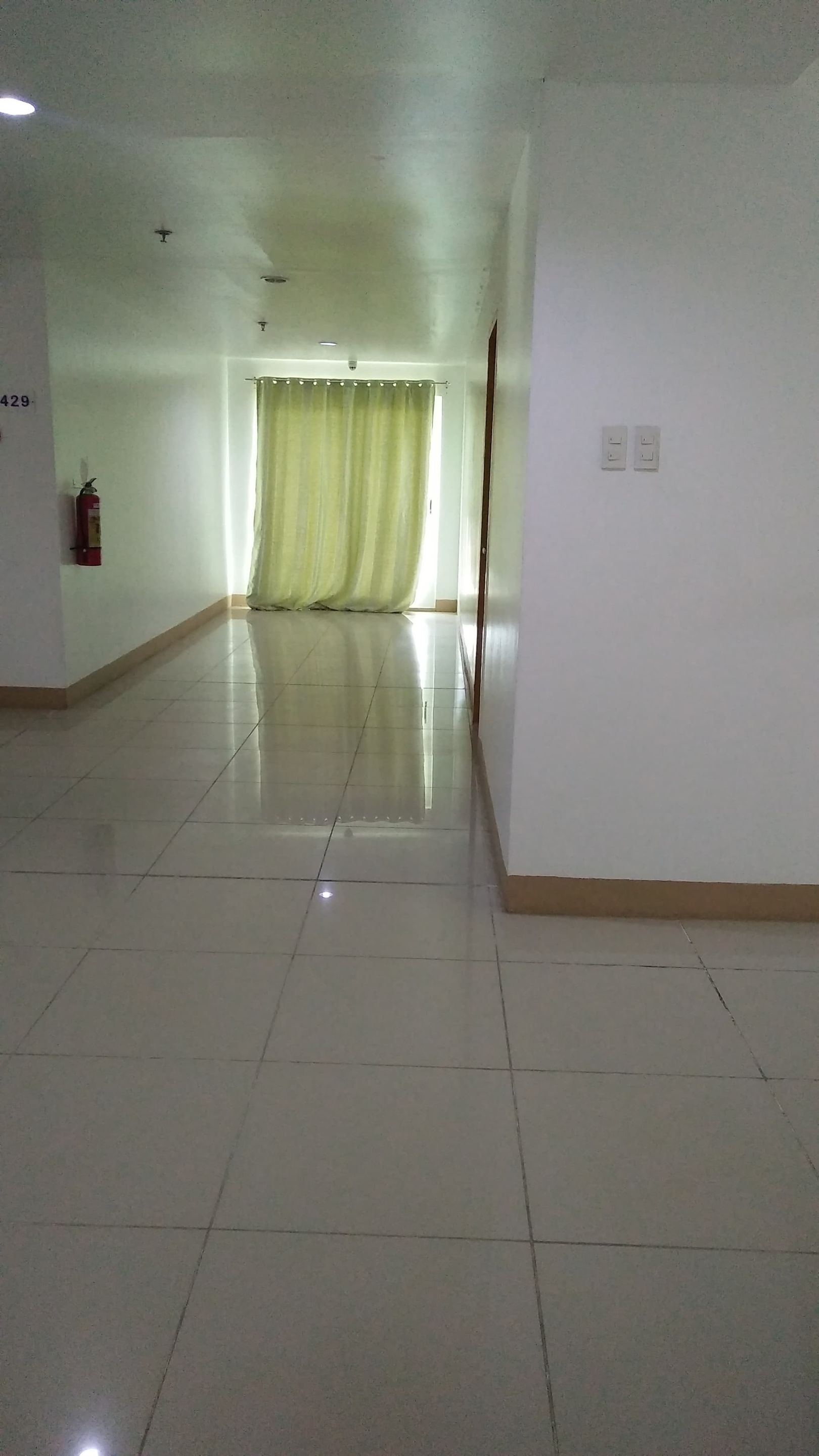 A spacious, empty hallway with a tiled floor, a fire extinguisher, and a curtain at the end.