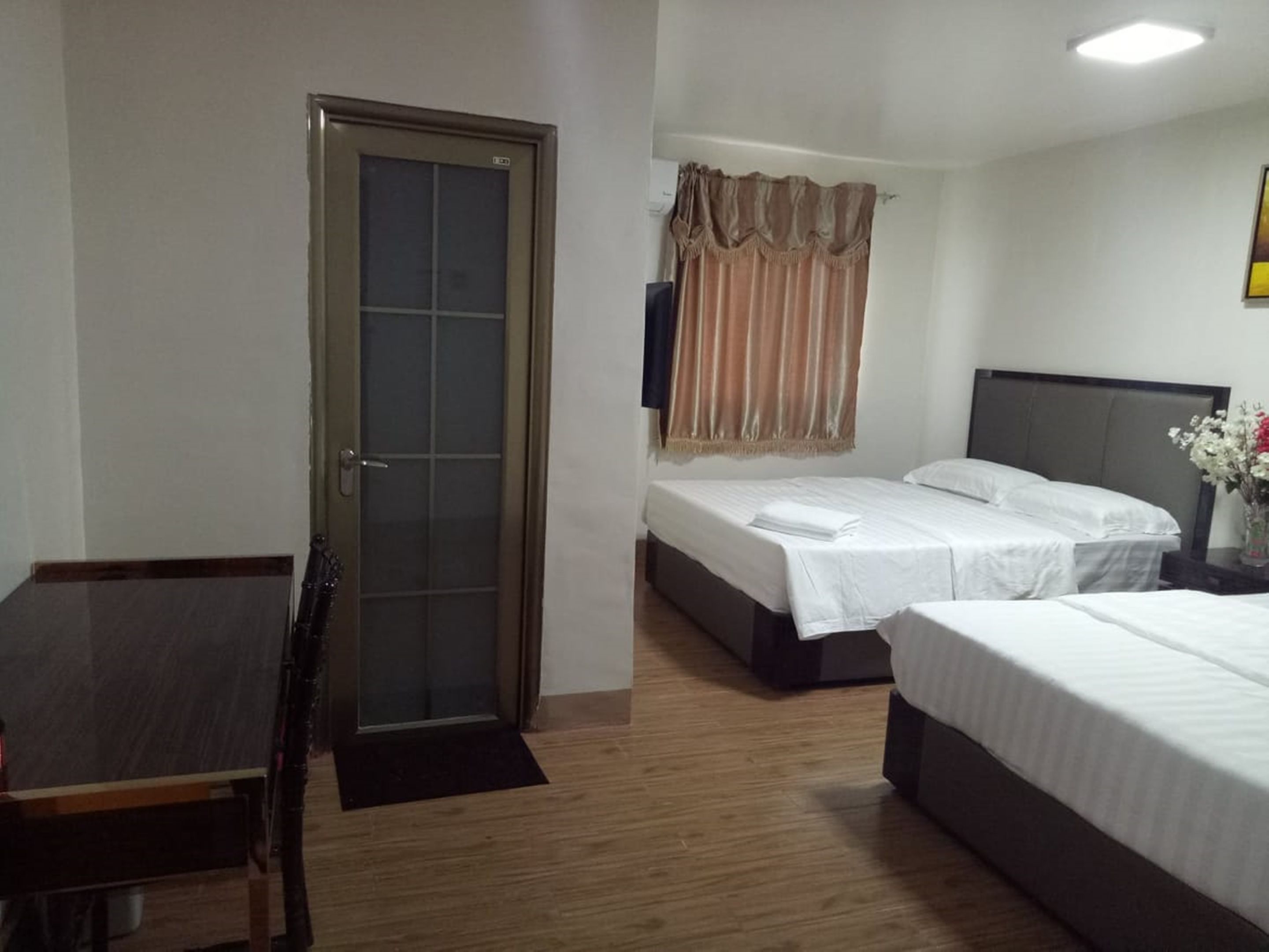 A hotel room with two beds, a desk, a chair, a door, and a window with curtains.