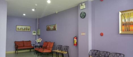 Uma área de recepção com paredes roxas, um extintor, um relógio e vários sofás e cadeiras.