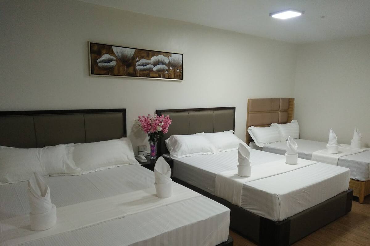 A hotel room with two single beds, a nightstand with a phone, a vase with flowers, and a painting on the wall.
