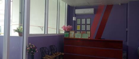 A reception area with a purple wall, a red counter, and a window with a view. There are two chairs and a potted plant.