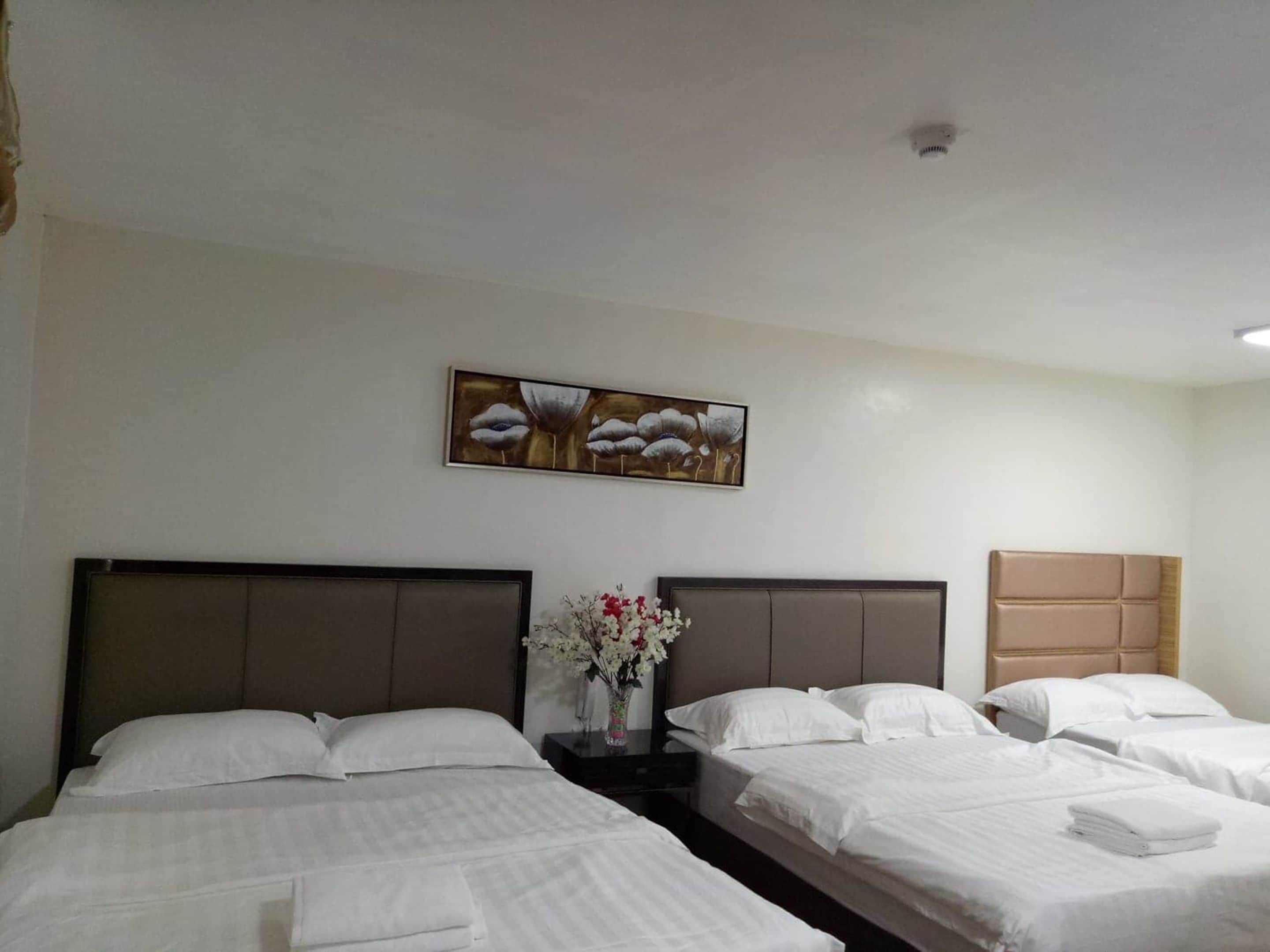 Habitación de hotel con dos camas, una mesita de noche con un jarrón de flores y un cuadro en la pared.