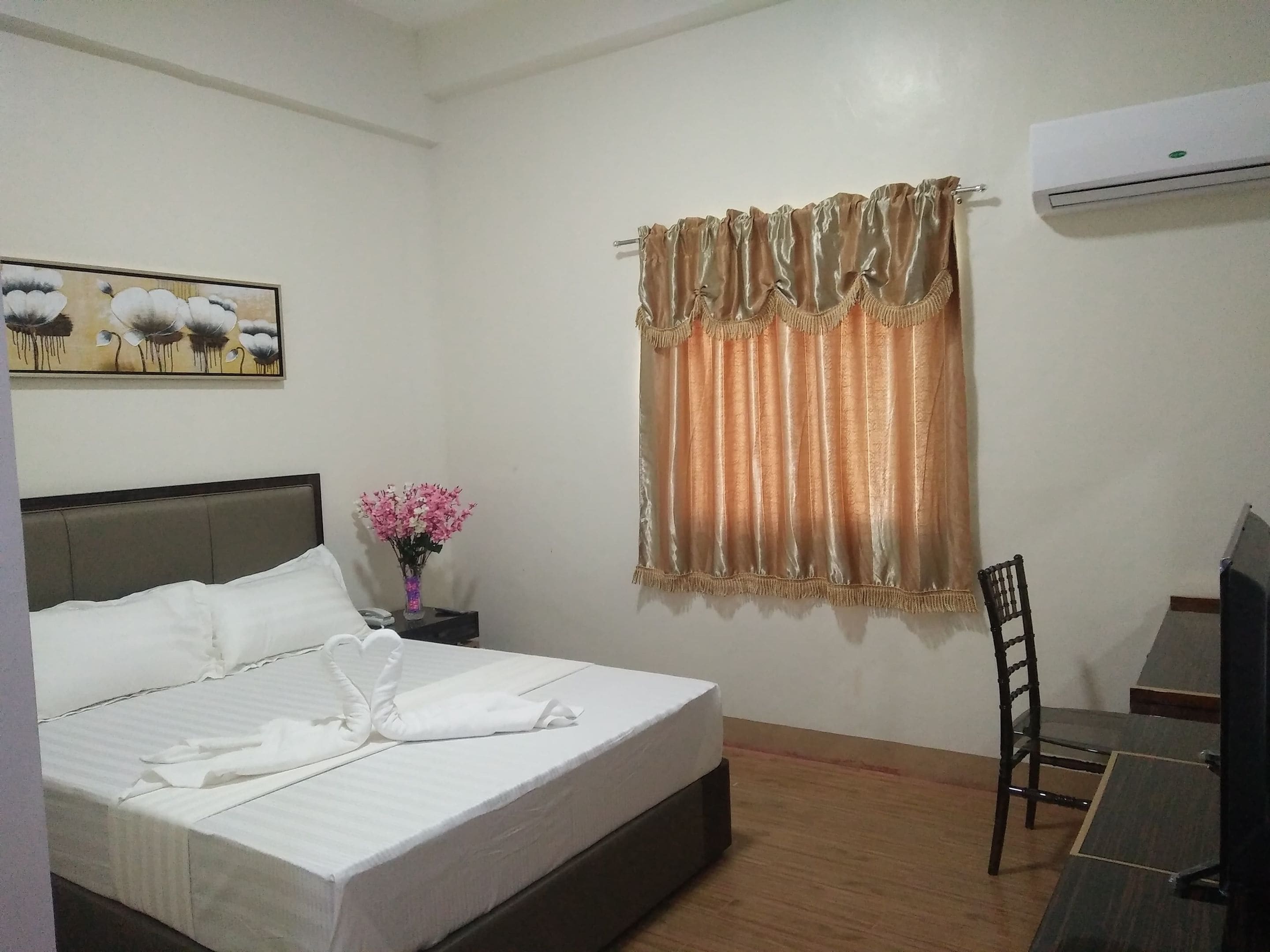 A hotel room with a bed, a nightstand with a vase of flowers, a chair, and a desk.