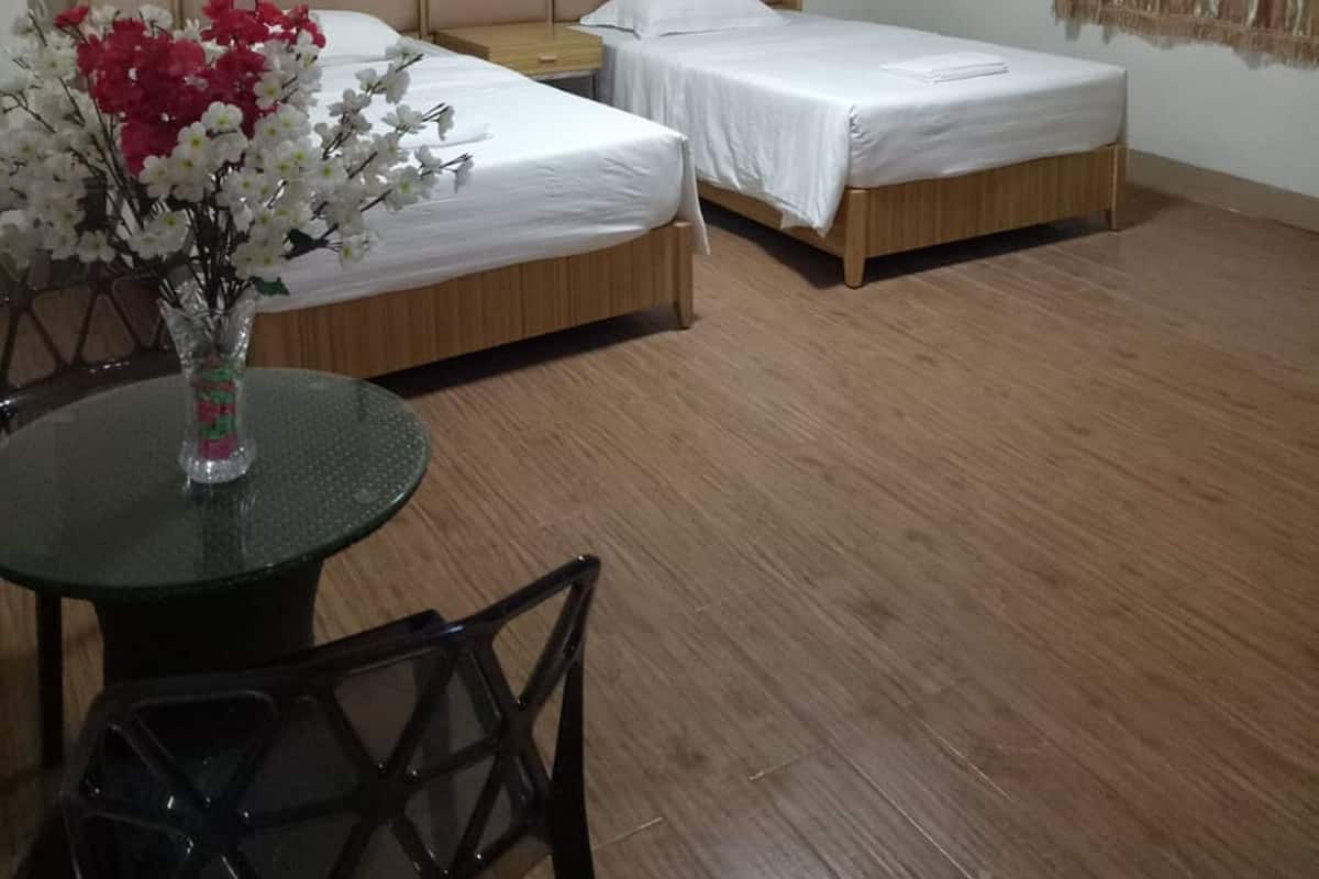 A hotel room with two beds, a small table with a vase of flowers, and a single chair.
